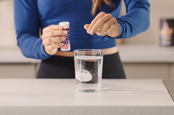 MaxiNutrition-Hydration-Tab-Frau-bereitet-Elektrolyt-Drink-im-Glas-zu
