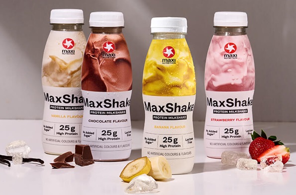 MaxiNutrition MaxShakes in vier verschiedenen Sorten vor der braunen Wand und mit Zutaten zu den jeweiligen Sorten.
