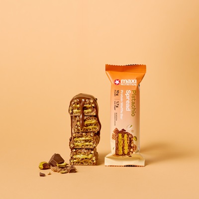 Protein Waffle Bar Pistachio Spread Packaging neben angeschnittenen Riegeln vor beigem Hintergrund