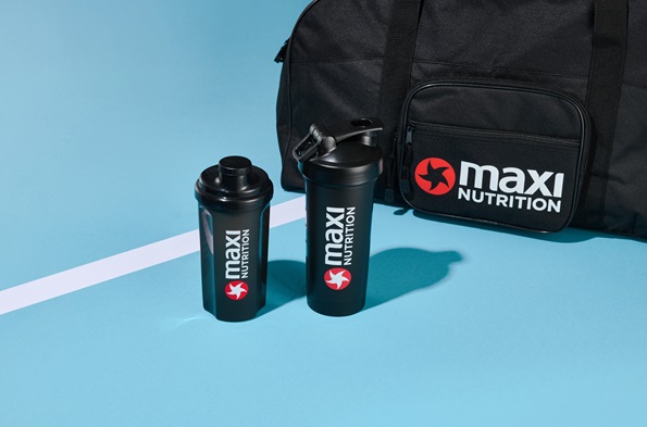maxinutrition-shaker-schwarz-500ml-vor-schwarzer-sporttasche-vor-blauem-hintergrund