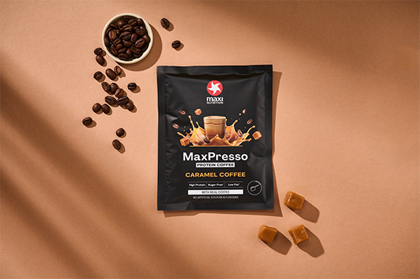 maxinutrition_MaxPresso_Caramel_Coffee_Sachet_liegend_auf_brauner_wand_neben_kaffeebohnen_und_karamel