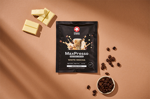maxinutrition_MaxPresso_white-mocha_Sachet_liegend_auf_brauner_wand_neben_kaffeebohnen_und_weißer_schokolade